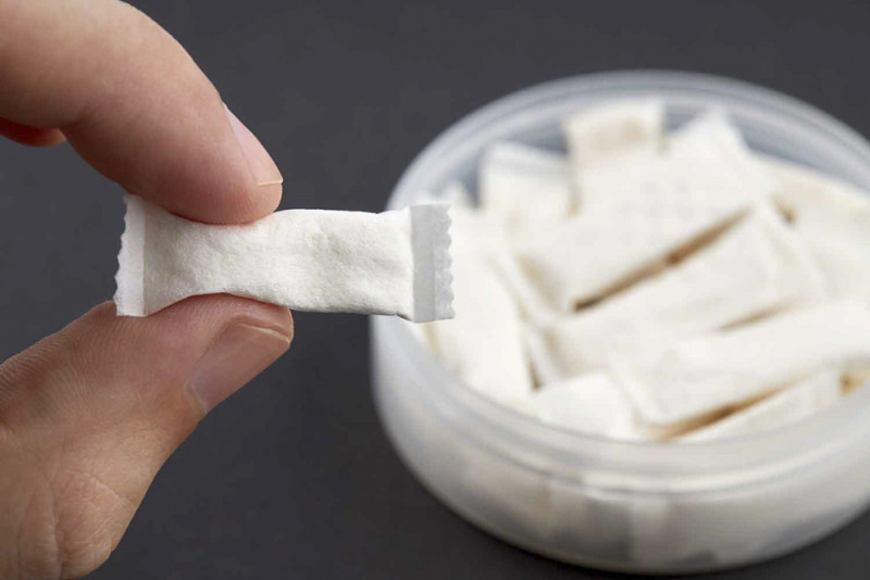 caucasian person holds snus tobacco pouch over black background.