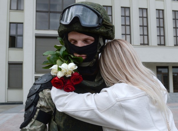 Kezében rózsákat tartó nő átölel egy rohamrendőrt Minszkben, 2020. augusztus 14-én