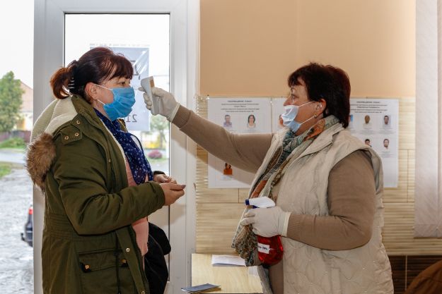 Egy helyi asszony testhőmérsékletét méri a válsztókerület munkatársa szavazás előtt az ukrajnai helyhatósági választásokon a kárpátaljai Zápszonyban