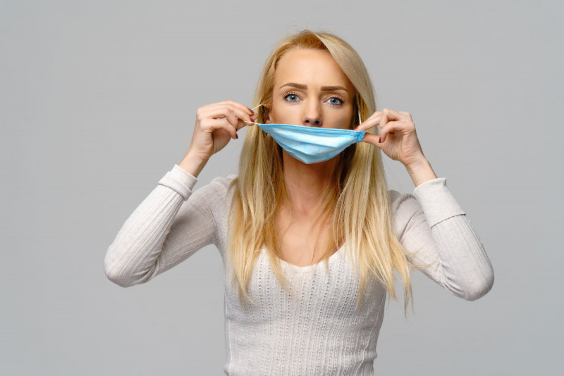 Studio portrait of young woman wearing a face protective mask isolated on gray background - flu virus epidemic protection, dust or pollen allergy, air pollution