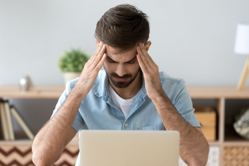 Tired man suffering from headache at work, massaging temples