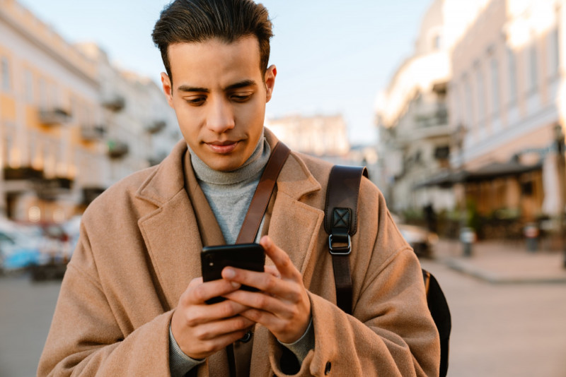 Young man wearing coat using mobile phone at city street